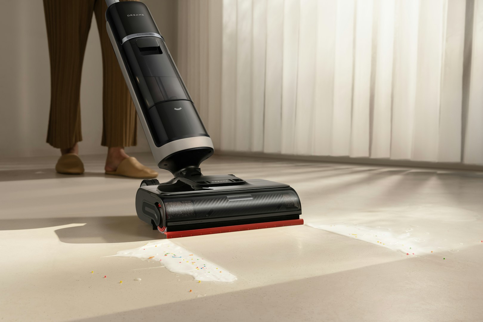 Two women in matching uniforms cleaning a modern indoor space with plants. One woman is using a vacuum while another in the background mops the floor. They are wearing gloves and the area is well-lit with a ladder visible in the background.